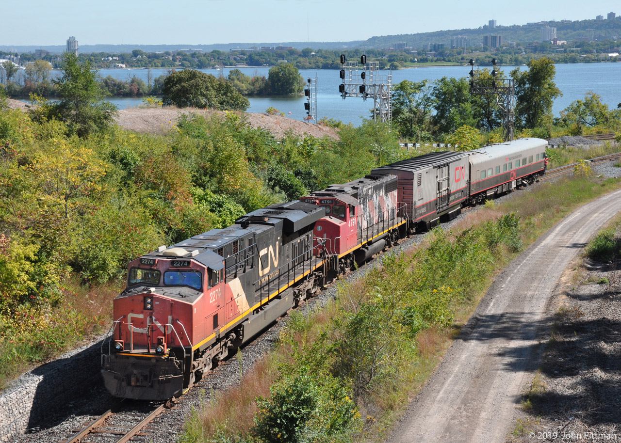 The CN TEST Track Evaluation System train that I saw September 11th was re-encountered on the 17th.  
It arrived at CN Bayview eastbound off the north track of the Dundas sub, continuing onto the Oakville sub. Later that afternoon it pushed back to Hamilton Jct, and returned westward via the Cowpath as seen here. Burlington Bay and western Hamilton are in the background.

The lead engine, ES44dc CN 2274 has a white rectangular box above its headlights which looks like an outdoor security camera, and a dashcam-like device inside the left cab window. GP38-2w CN 4791 has a squarish box on the nose beside the C of CN, with a cable running back to the boxcar. 
The modified boxcar is CN 414852 "DGRMS Test Car". The TEST Track Evaluation System coach is CN 1057.